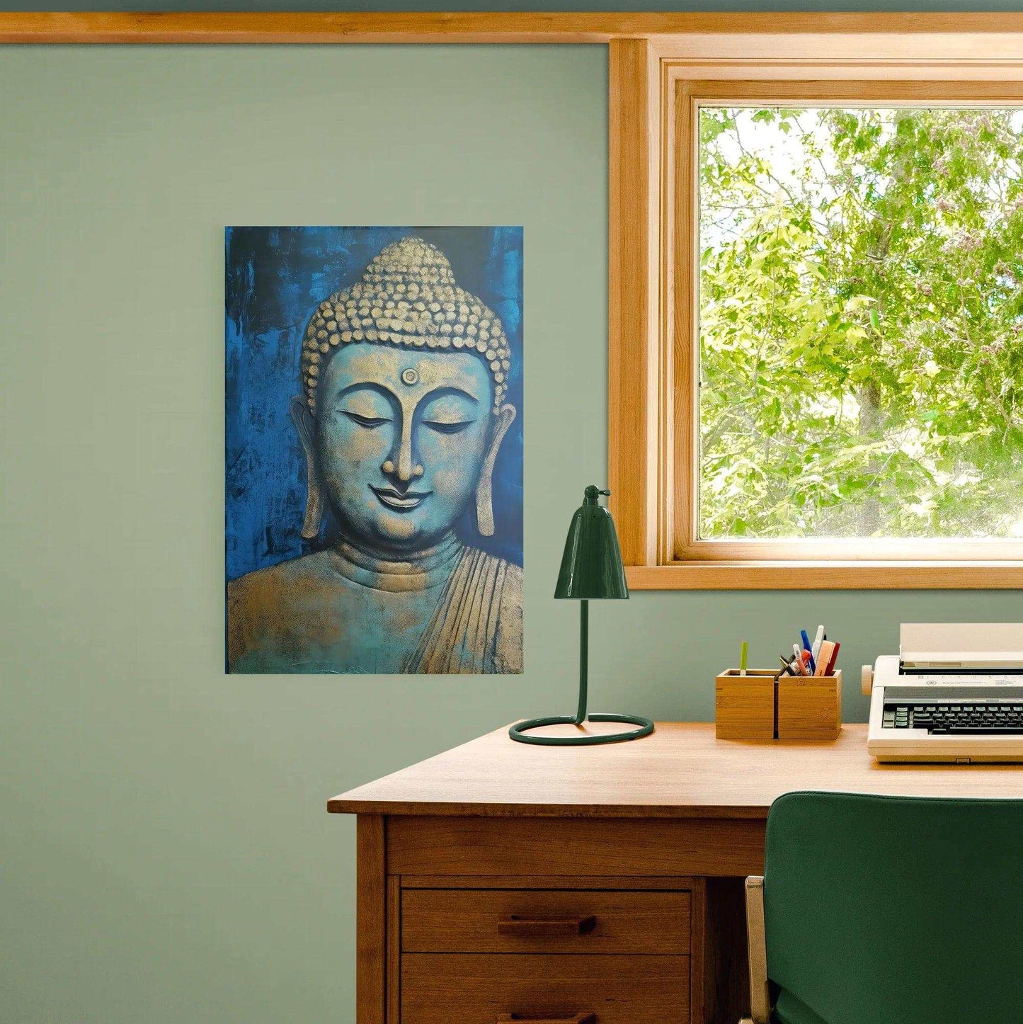 In a home office setting, a calming blue and gold Buddha painting is displayed on a mint green wall, beside a wood-framed window that looks out to lush greenery, harmonizing with the wooden furniture and green desk lamp.