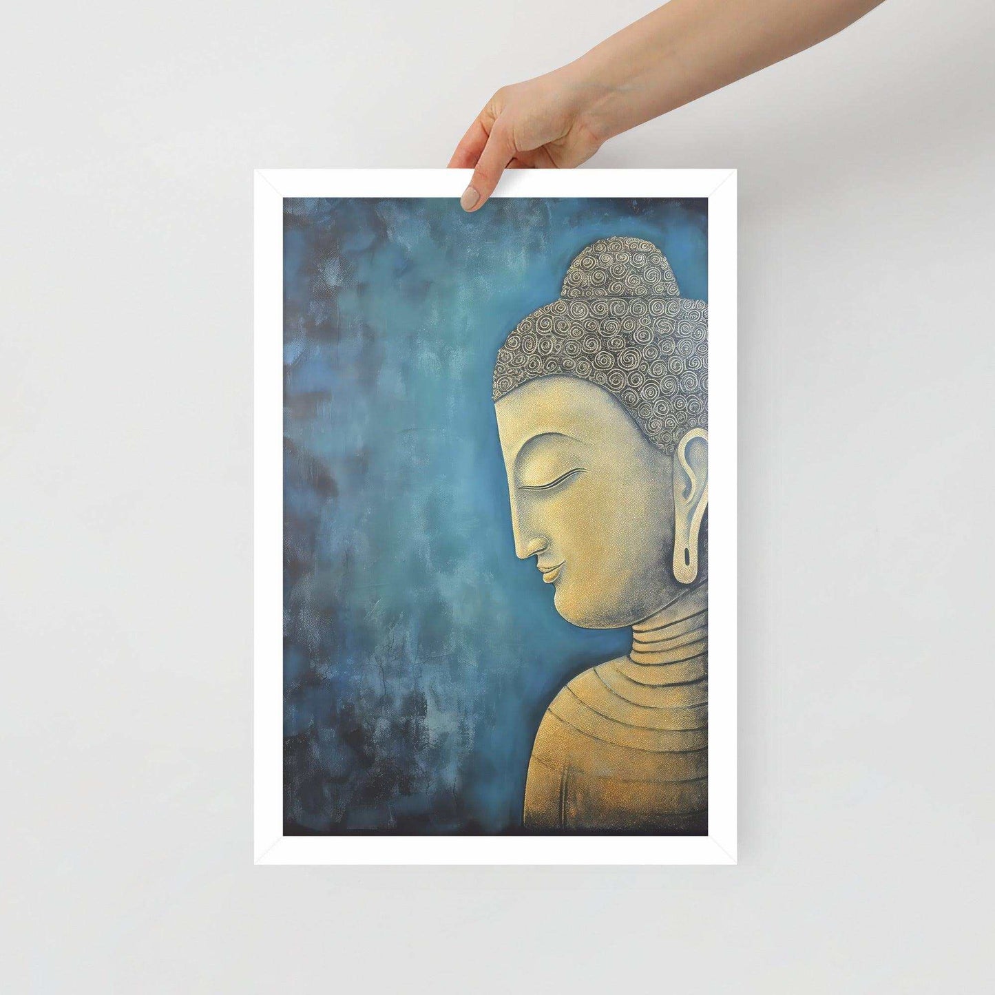 A hand is placing a framed poster on a white background, where a serene Golden Buddha Art with a patterned head and golden features is portrayed in profile against a mottled blue backdrop, all within a white oak frame.