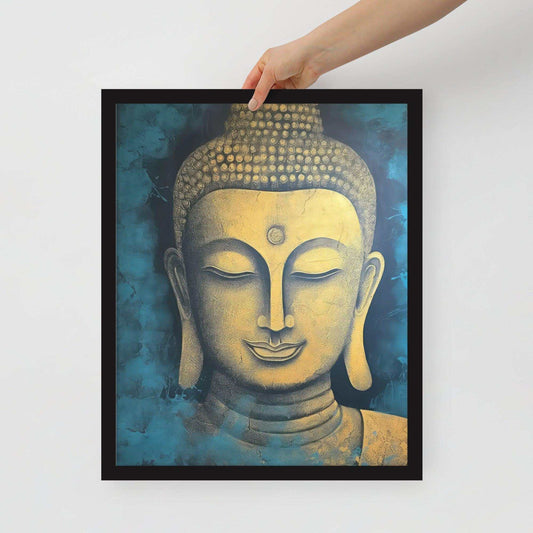 A hand is holding a black-framed poster of a golden Buddha head with a tranquil expression, adorned with intricate details against a mottled blue background, combining a sense of peace with artistic texture.