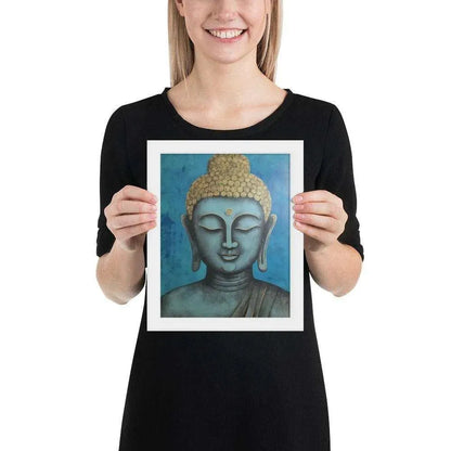 A beaming woman is holding a white-Happy Buddha Framed Print that features a Buddha head painted in shades of blue and gold against a textured blue background, exemplifying a fusion of traditional iconography with a modern artistic twist.