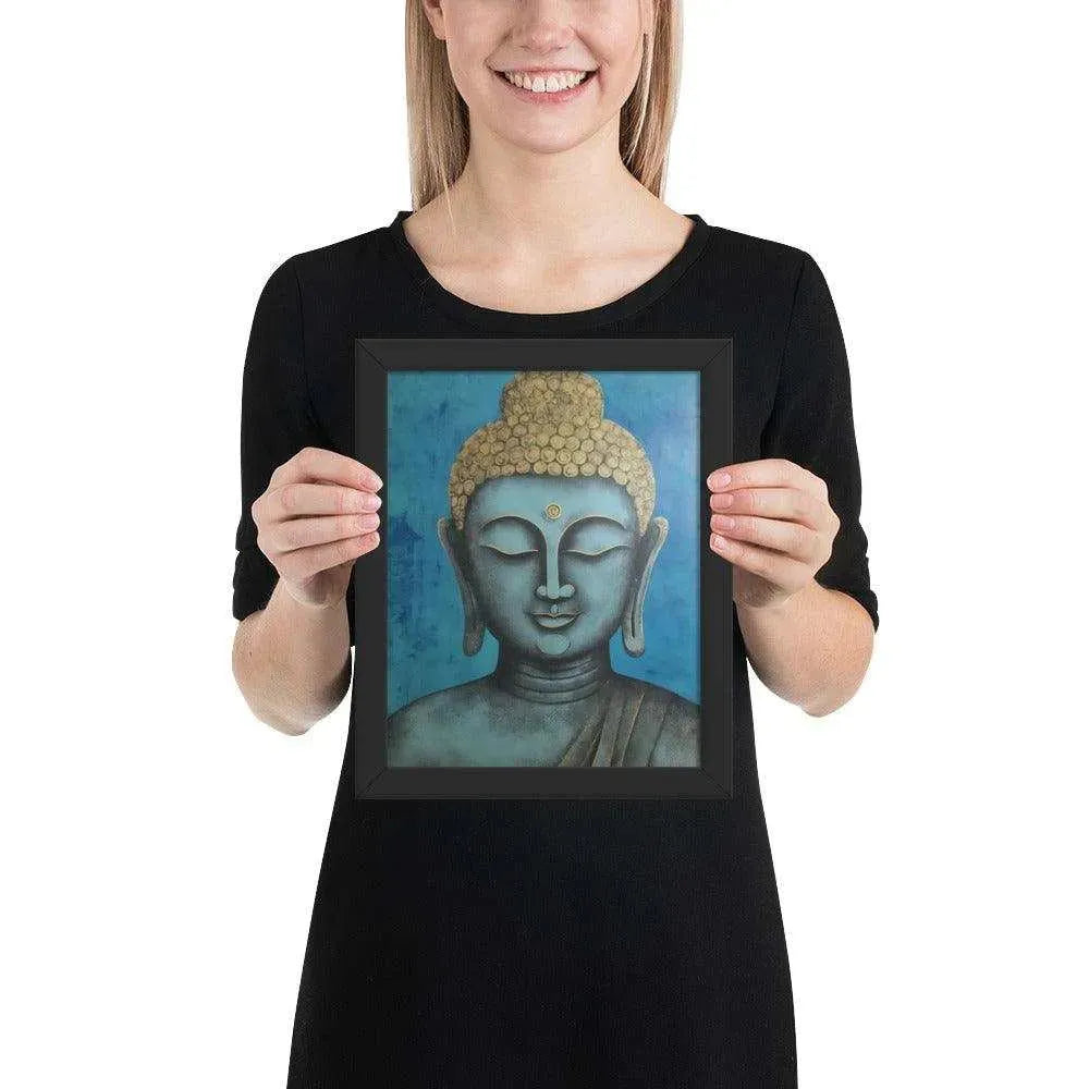 A beaming woman is holding a black-Happy Buddha Framed Print that features a Buddha head painted in shades of blue and gold against a textured blue background, exemplifying a fusion of traditional iconography with a modern artistic twist.