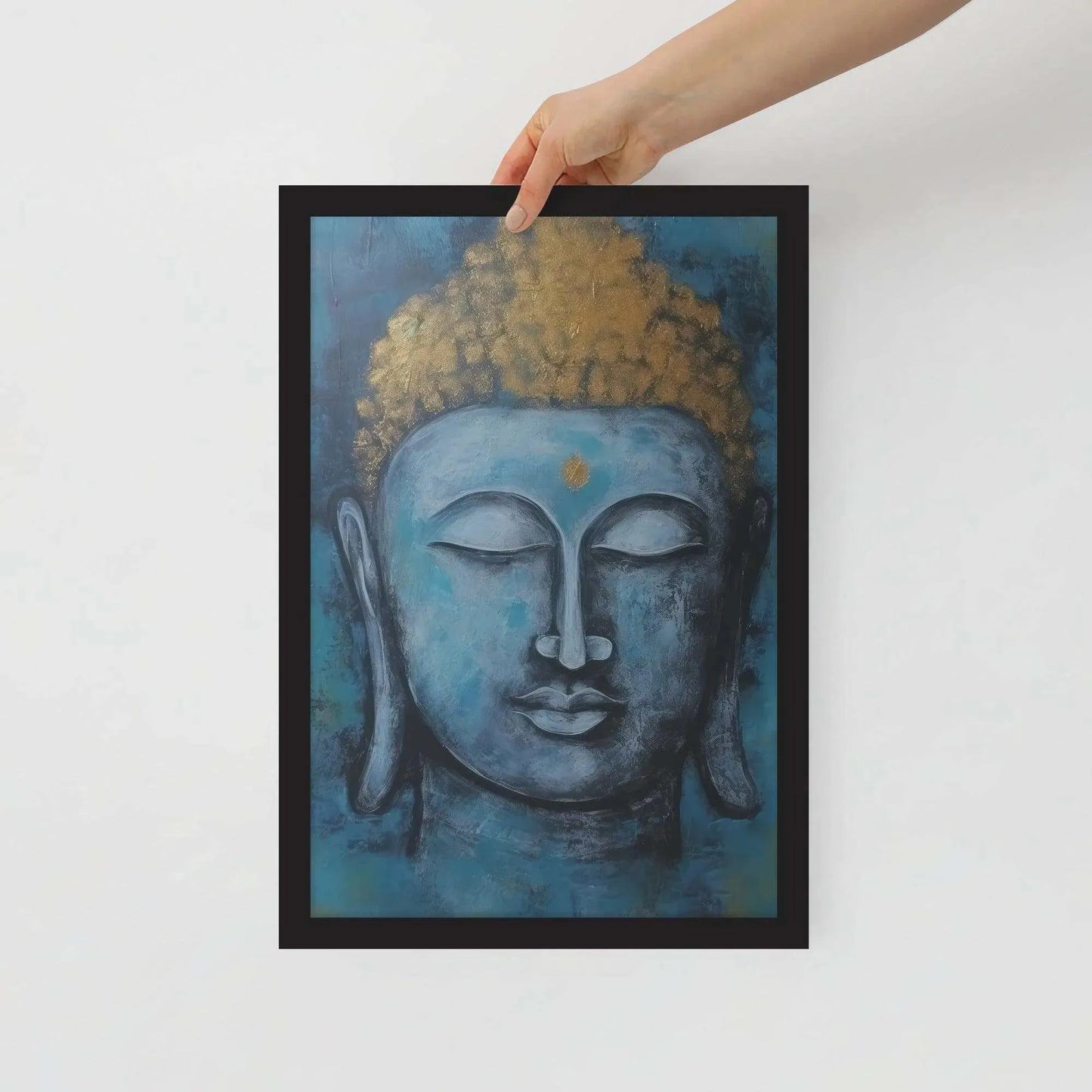 A hand is adjusting a framed poster with a black oak finish depicting a blue Buddha head with a textured gold leaf crown against a blue background, giving the impression of tranquility and artistic simplicity against a white backdrop.