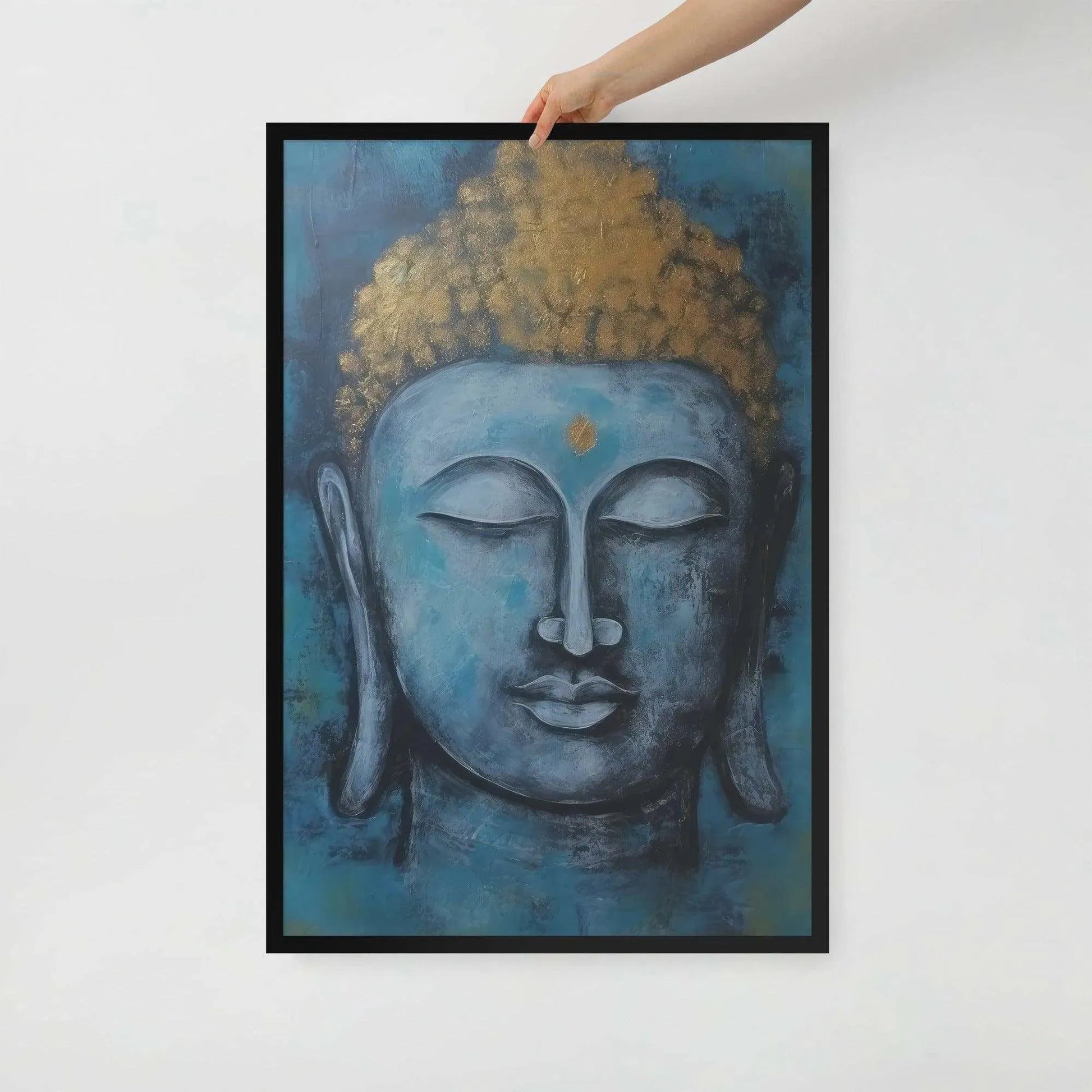 A hand is adjusting a framed poster with a black oak finish depicting a blue Buddha head with a textured gold leaf crown against a blue background, giving the impression of tranquility and artistic simplicity against a white backdrop.