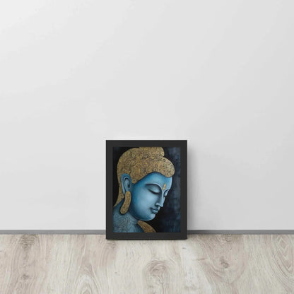 A framed Tibetan Blue Buddha Painting depicts a side profile of a serene, blue-toned Buddha with a golden patterned head, highlighted with a delicate golden ornament on the forehead. The artwork is placed against a dark, smokey background within a black oak frame, resting on a light wooden floor next to a white wall.