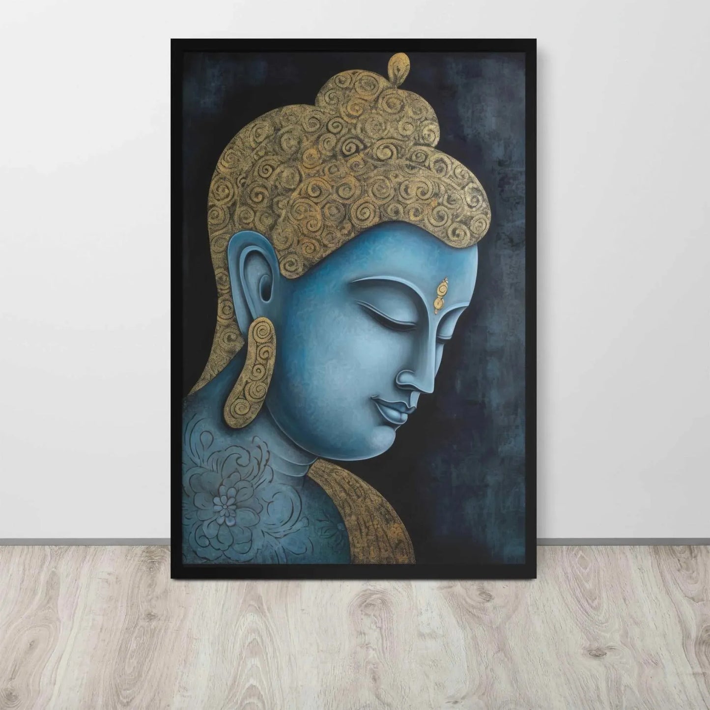 A framed Tibetan Blue Buddha Painting depicts a side profile of a serene, blue-toned Buddha with a golden patterned head, highlighted with a delicate golden ornament on the forehead. The artwork is placed against a dark, smokey background within a black oak frame, resting on a light wooden floor next to a white wall.