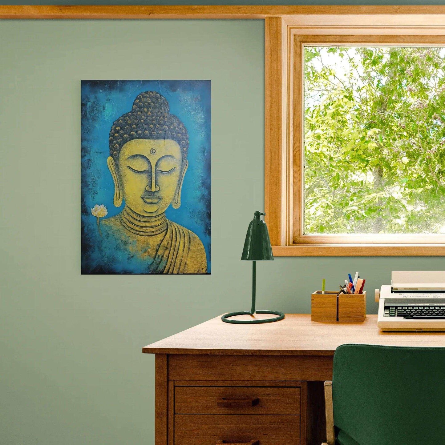Tranquil blue and gold Buddha portrait mounted on a sage green wall beside a window with a view of lush greenery, complementing a classic wooden desk with a typewriter, lamp, and office supplies, creating a serene workspace.