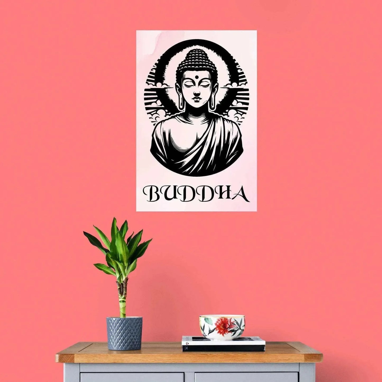 The Timeless Buddha Poster by Printify, featuring a black and white illustration, adorns a pink wall and exudes spiritual serenity. Below it sits a wooden table displaying a potted plant and a teacup. The word "Buddha" is elegantly scripted beneath the tranquil design.