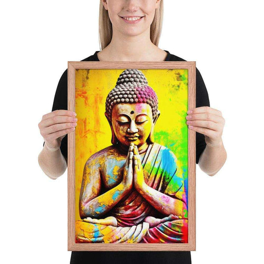 A smiling woman holds a Vibrant Buddha Framed Art showing a Buddha statue in a prayer pose, with a vividly painted, multicolored background. The Buddha's head is adorned with a pinkish hue, contrasting with the yellow and blue tones of the body and background. The natural red oak frame complements the warm colors of the artwork.